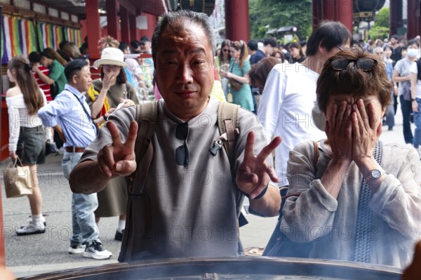 Visitors to Senso-ji Temple pose in front of a large fire bowl, Tokyo, Japan