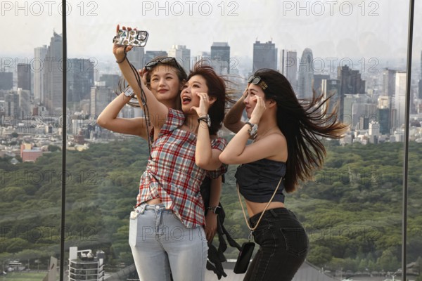 Three woman take a selfie with a view of Tokyo skyline, Tokyo, Japan
