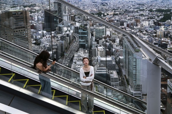 Women ride the escalator in Shibuya with sweeping views over Tokyo, Tokyo, Japan