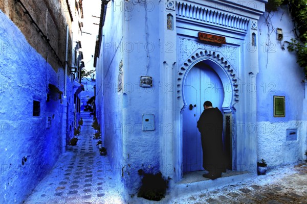 Blue alley with traditional Moroccan gate and a person in the medina of Chefchaouen, Chefchaouen, Tanger-Tetouan, Morocco