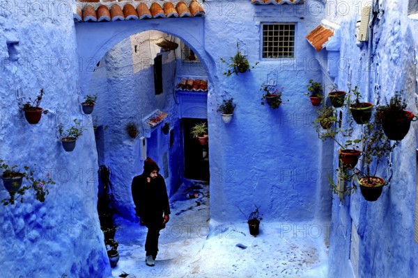 Blue alley with arches and flower pots interspersed with a passing person in the Medina, Chefchaouen, Tanger-Tetouan, Morocco