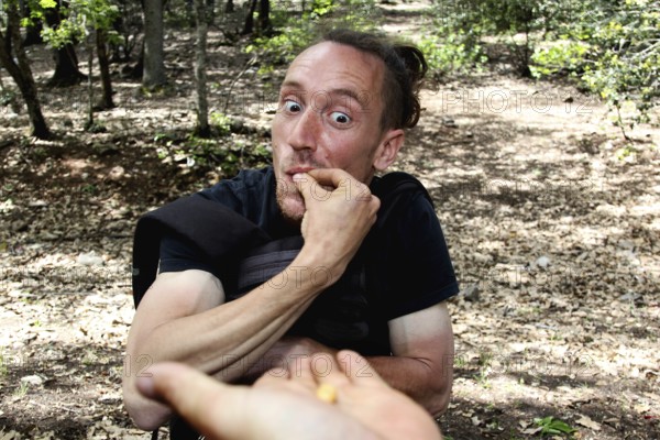 Man eats with an amused hand gesture in the forest, Azrou, Forèt des Cèdres, Morocco