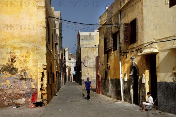 Sunlit narrow alley with passer-by and old buildings, El Jadida, Cité Portugaise, Morocco