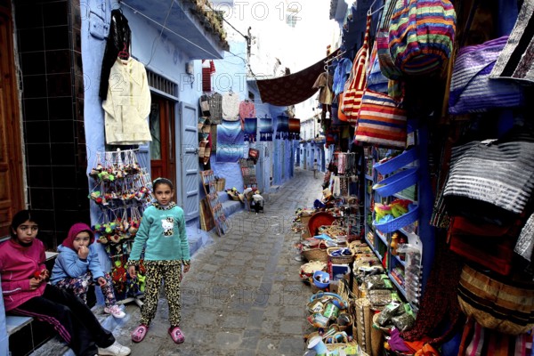 Alley in the medina of Chefchaouen with colorful goods and children playing, Chefchaouen, Morocco