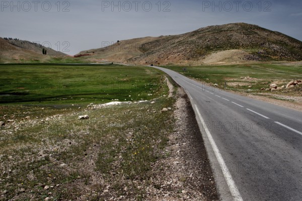 An asphalted road runs through the green and hilly countryside of Col Ouzad, Col Ouzad, Béni Mellal-Khénifra region, Morocco