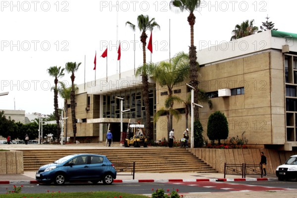 Modern building in Agadir with palm tree decoration, flags and a passing car, Agadir, Morocco