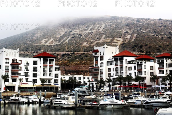 The marina of Agadir with modern buildings in front of a hill with lettering, Agadir, Morocco