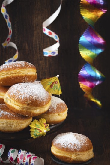 A pile of donuts with powdered sugar, colorful garlands and streamers against a dark wooden background, carnival