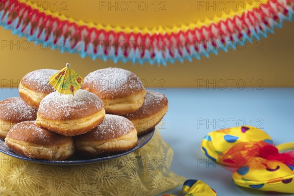 A plate of donuts with powdered sugar on a table surrounded by colorful carnival decoration