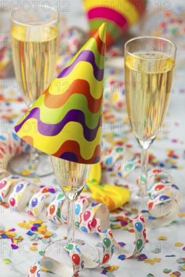 Champagne glasses with colorful party hat surrounded by confetti and streamers, carnival