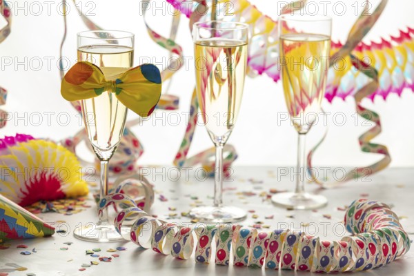 Three champagne glasses decorated with bows, surrounded by colorful confetti and streamers, carnival