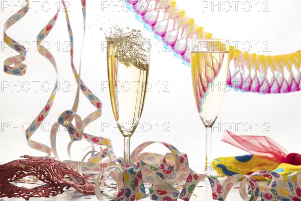 Two champagne glasses, one sparkling, in a lively atmosphere with streamers and a mask, carnival