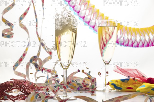 Two champagne glasses, one sparkling, in a lively atmosphere with streamers, confetti and mask, carnival