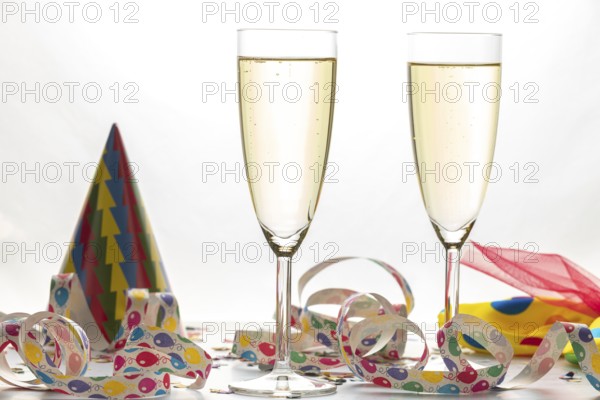 Two filled champagne glasses next to colorful streamers and party hat, carnival