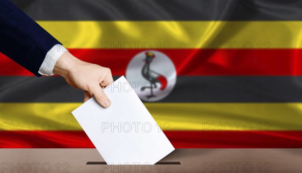 Hand placing a ballot in ballot box with the Ugandan flag in the background. Uganda presidential vote