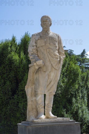 Stone statue of a man in uniform in front of a green hedge outdoors, Stalin monument, sculpture, Gori, Inner Kartli region, Georgia