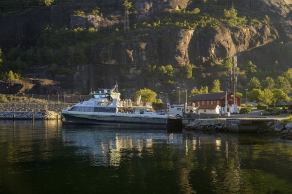 Kulumbus ferry from Lysebotn to Stavanger is located in Lysebotn harbour in front of rocky mountains, illuminated by warm sunlight, Lysebotn, Rogaland Municipality, Norway