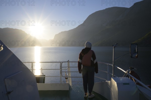 Person standing alone on a ferry at sunset with view of fjord and mountains, view from Columbus ferry, Lysefjord, Rogaland, Norway