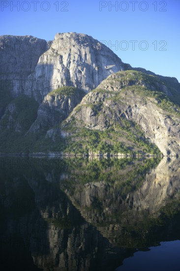 Majestic rocks reflected in clear water under a bright blue sky at Lysefjord, Rogaland, Norway