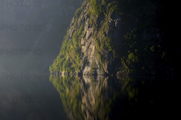 A steep rock rises up, its massive presence reflected in still water, Lysefjord, Rogaland, Norway