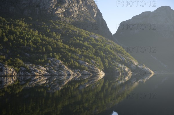 Pristine nature with wooded cliffs reflected in the tranquil Lysefjord, Lysefjord, Rogaland, Norway