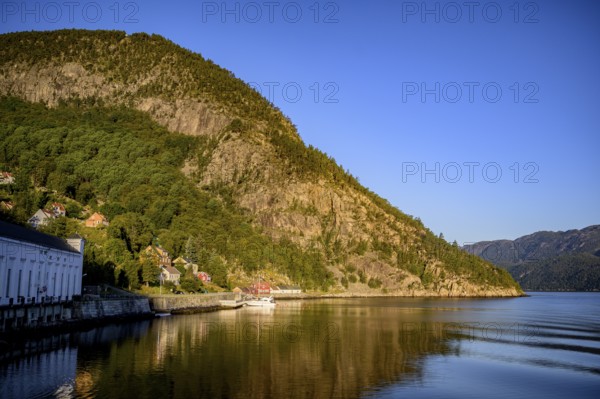 A peaceful stretch of Lysefjord with mountains and a picturesque village on the shore, view from the Columbus ferry, Lysefjord, Rogaland, Norway