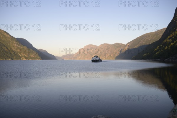 Columbus shipping company ferry in the middle of the quiet Lysefjord at dusk surrounded by mountains, Lysefjord, Rogaland, Norway