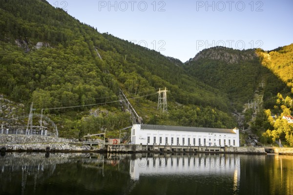 A power plant stands on the banks of a calm body of water de, Lysefjord, nestled in green wooded mountains