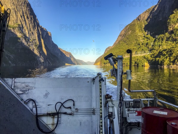 Lysebotn, Rogaland Municipality, Norway, View from a boat of the sunny Lysefjord surrounded by high mountains, A boat moves through a quiet fjord between steep mountains under clear skies