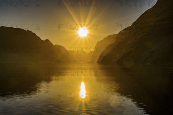 Atmospheric star-shaped sunlight is reflected on quiet fjord waters of Laysefjord between massive rock walls, view from Columbus ferry, Lysefjord, Rogaland, Norway