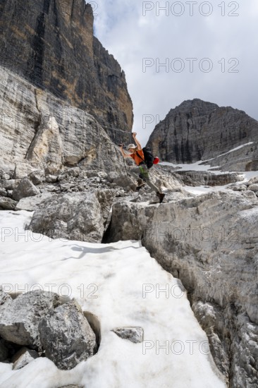 Mountaineer jumping off a rock into the snow, Camosci Valley, Brenta Mountains, Brenta-Adamello Natural Park, Trentino, Italy