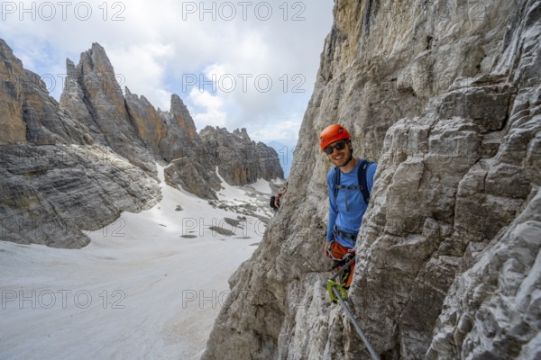 Mountaineer climbs on a steep rock face in the Via Ferrata dell'Ideale via ferrata, spectacular mountain landscape with steep rock faces, remnants of the Vedretta d'Ambiez glacier in the back, Brenta Mountains, Brenta-Adamello Nature Park, Trentino, Italy