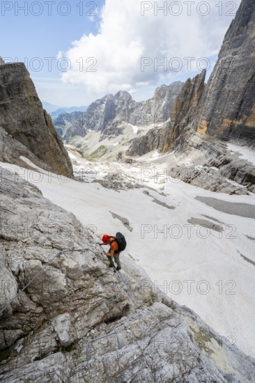 Mountaineer climbs on a steep rock face in the Via Ferrata Brentari via ferrata, spectacular mountain landscape with steep rock faces, remains of the Vedretta d'Ambiez glacier in the back, Brenta Mountains, Brenta-Adamello Nature Park, Trentino, Italy