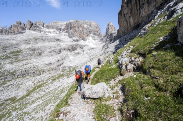 Three mountaineers on a hiking trail to Sella della Tosa, mountainous landscape in the Brenta Mountains, Brenta-Adamello Natural Park, Trentino, Italy