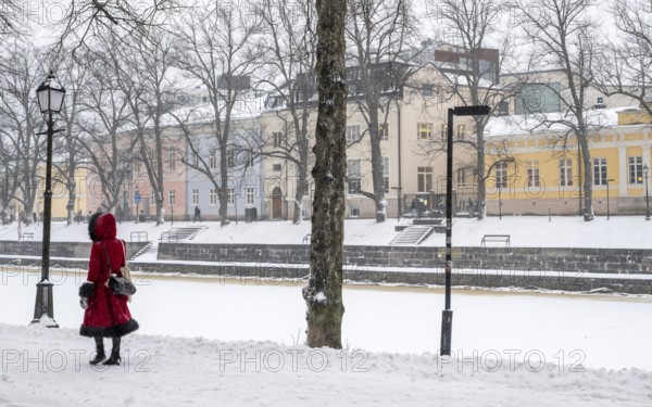 Woman in red winter coat walks along the frozen Aurajoki river, wintery Turku or Swedish Åbo, Varsinais-Suomi, Finland