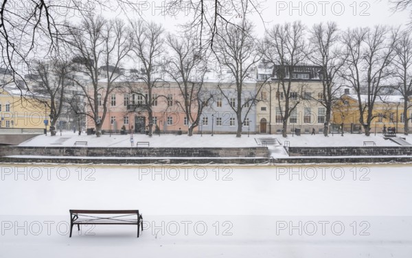 Bench, historic buildings on the frozen Aurajoki River, wintery Turku or Swedish Åbo, Varsinais-Suomi, Finland
