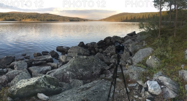Drevsjø, Innlandet, Norway, scene of a photographer on a rocky lakeside at sunset, Gutulia National Park, Engerdal, Innlandet, Norway
