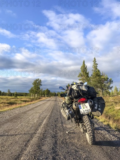 Idre, Dalarnas län, Sweden, BMW G 650 GS Sertao enduro motorcycle with complete camping equipment stands on a gravel road with blue sky and evening light