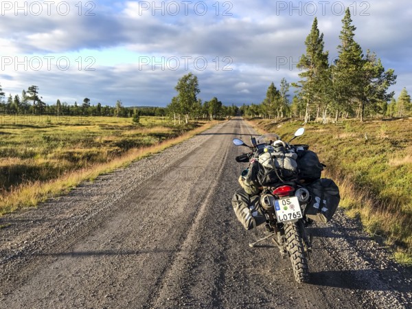 Idre, Dalarnas län, Sweden, BMW G 650 GS Sertao enduro motorcycle with full camping equipment on a country road at sunset with forest landscape
