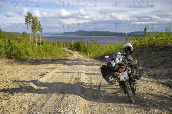 Lövdalen, Jämtland County, Sweden, A dirt road leads through slightly wooded terrain with a BMW G 650 GS Sertao enduro motorcycle and lake in the background