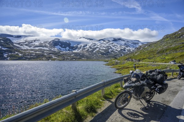 Geiranger, Møre og Romsdal Province, Norway, BMW G 650 GS Sertao Enduro motorcycle trip along a lake with snow-covered mountains under a blue sky