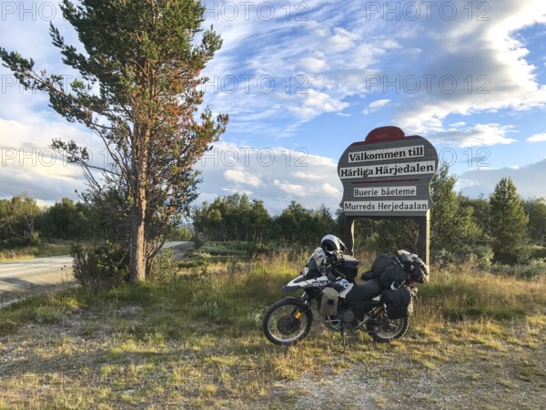 Funäsdalen, Jämtlands län, Sweden, Rural scene with a BMW G 650 GS Sertao Enduro motorcycle next to a welcome sign Wonderful Herjedalen under a clear sky