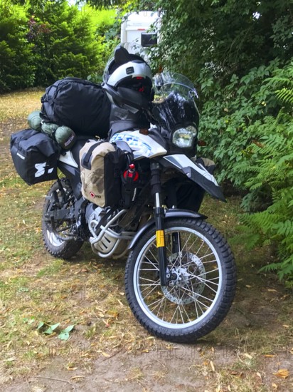 Bad Bramstedt, Schleswig-Holstein, Germany, loaded BMW G 650 GS Sertao Enduro motorcycle with camping equipment in the shade of tall trees on grassy ground