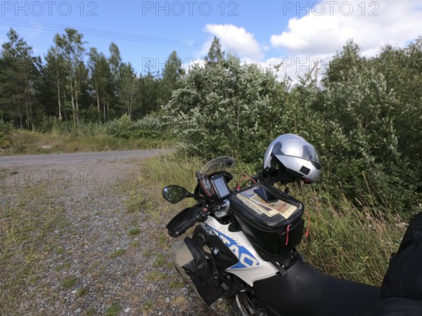 Vikbolandet, Östergötlands län, Sweden, BMW G 650 GS Sertao enduro motorcycle with helmet tank bag and saddlebags and GPS device on a rural road surrounded by trees under cloudy sky