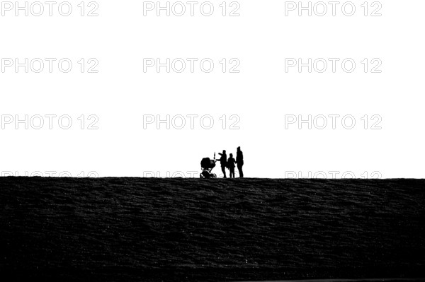 Silhouette of family walking with stroller on grassy dike at Jade Bay, Wadden Sea National Park, Jade Bay, Dangast, Varel, Lower Saxony, Germany
