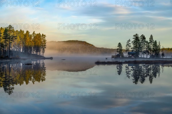 Calm lake with trees and hills in morning fog, picturesque and peaceful atmosphere