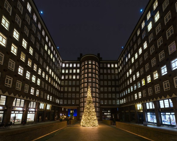 A festively lit Christmas tree stands in the courtyard between symmetrical buildings
