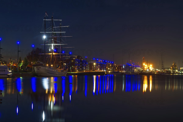 Nocturnal harbor with illuminated sailing ship and reflections in calm water