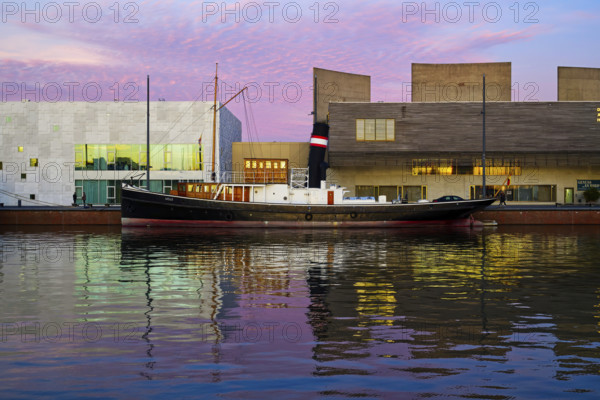 Harbour with illuminated tugboat and evening sky in shades of pink and blue