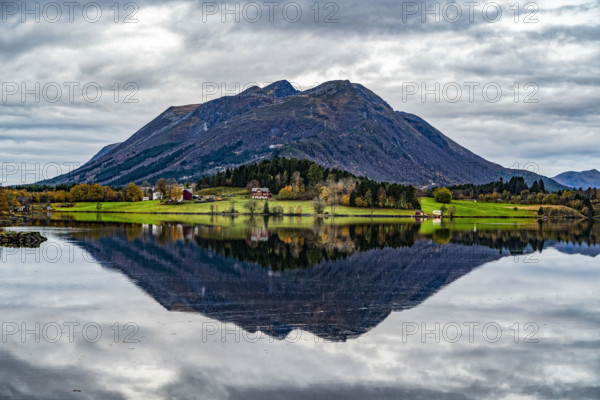 A lake reflects the autumn colors of meadows and mountains under a cloudy sky